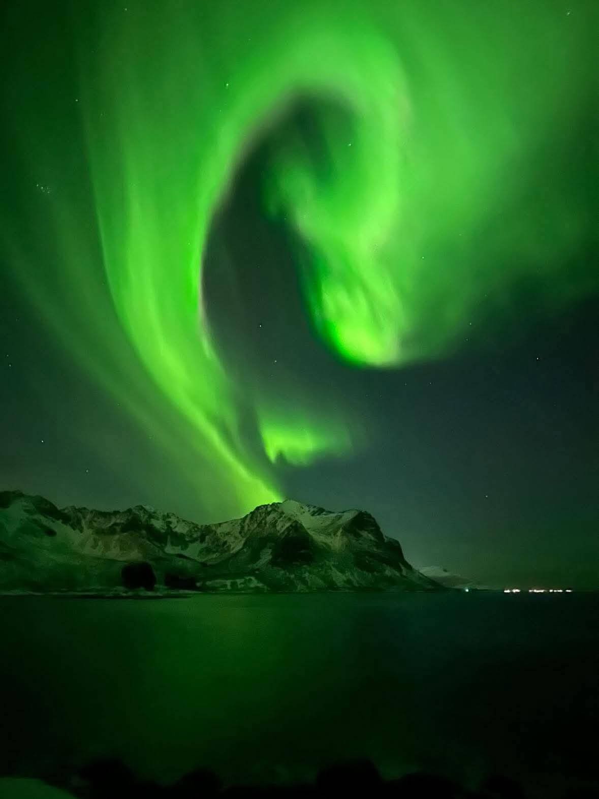 Northern lights glowing over mountains and water at night