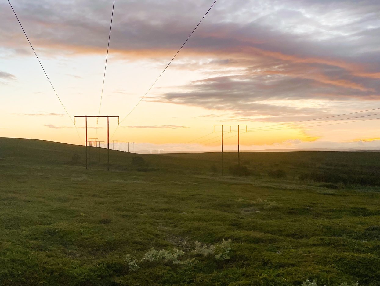 Kraftledninger krysser det åpne landskapet ved Varangerbotn i solnedgang