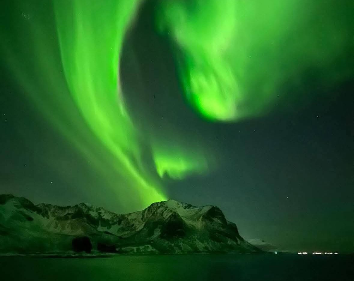 Northern lights glowing over mountains and water at night