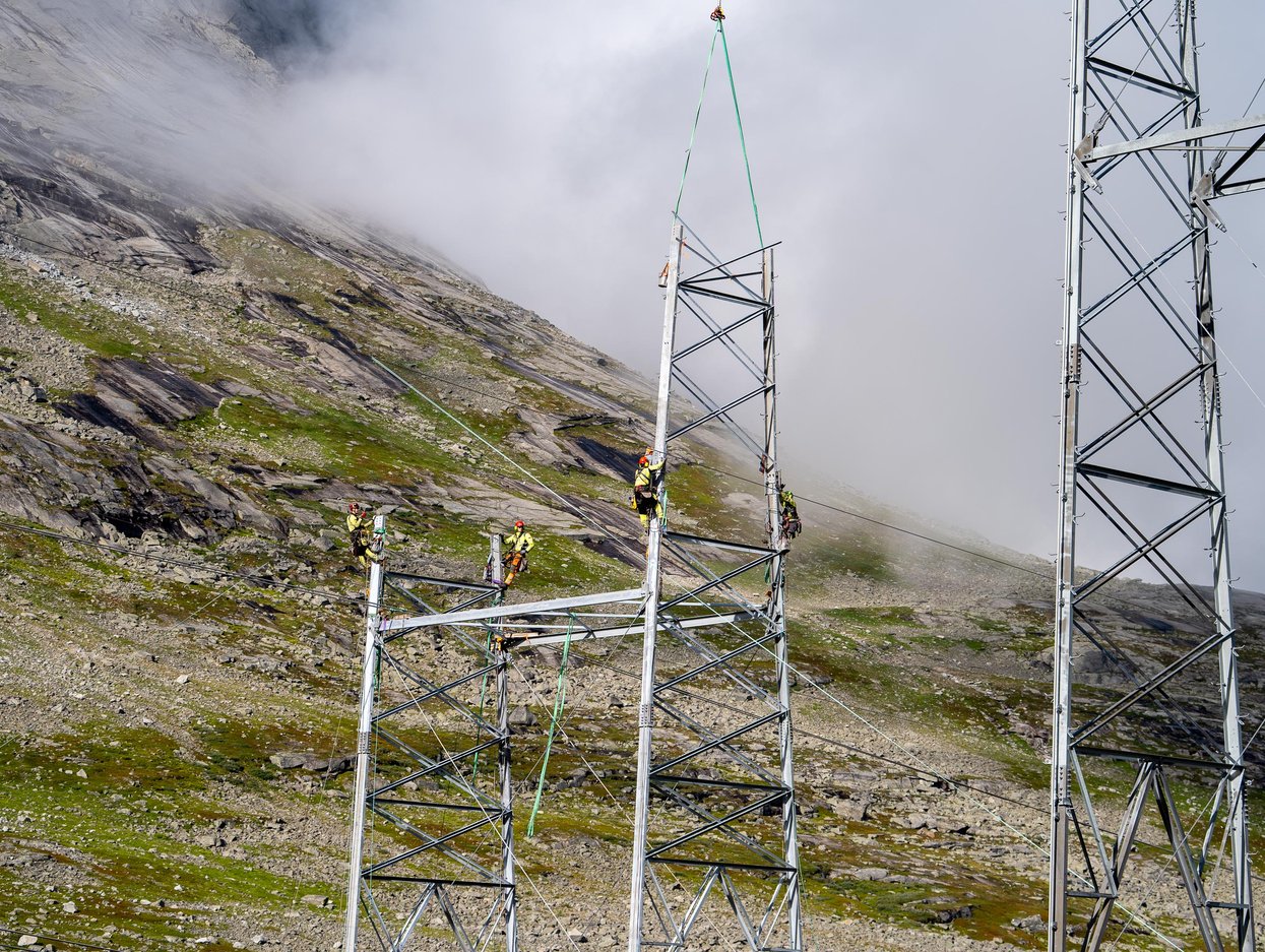 Bilde av høyspentmast og folk som jobber i masta.