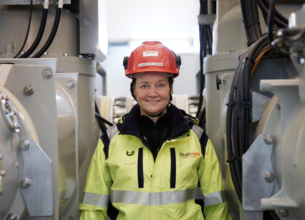 Elisabeth Vike Vardheim in high-visibility clothing and helmet standing between technical equipment at a facility