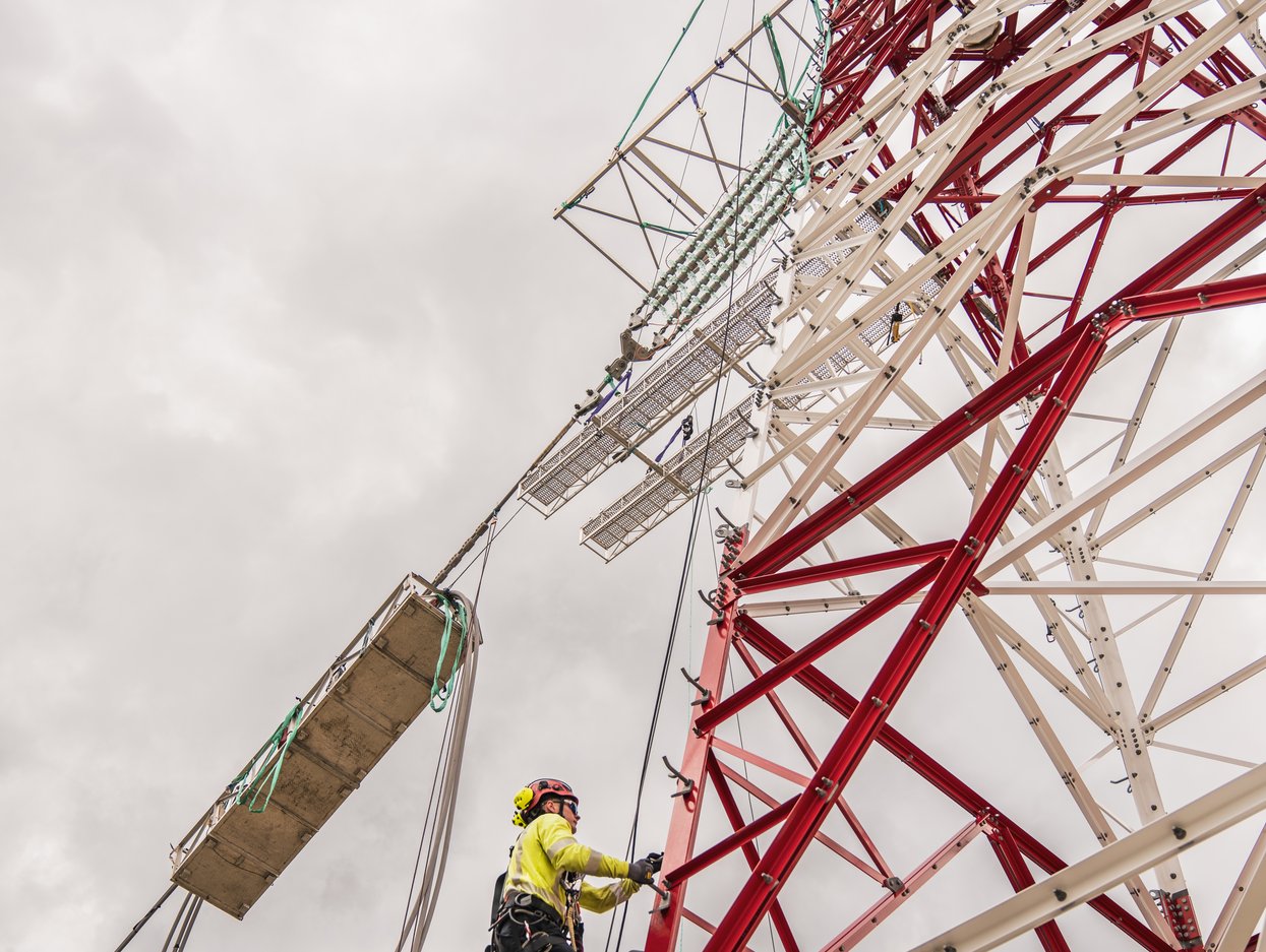 Worker climbing a red and white transmission tower during line installation