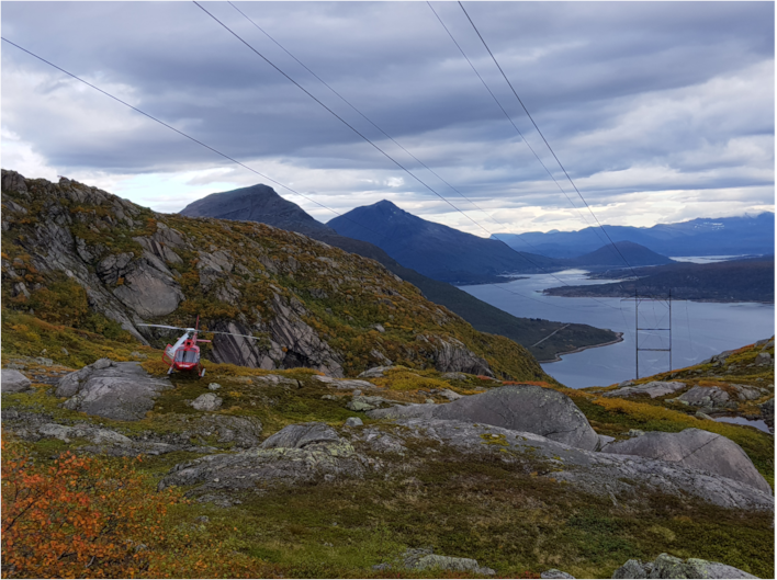 Illustrasjon av helikopter på toppen av et fjell med fjord i bakgrunnen