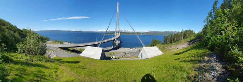 Bro i havet med fjell med snø rundt. 