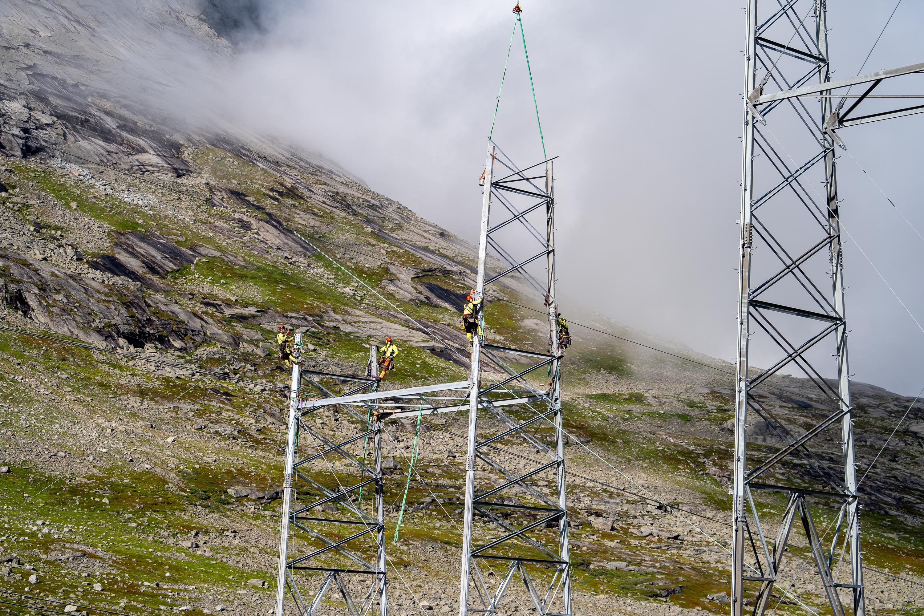 Bilde av høyspentmast og folk som jobber i masta.